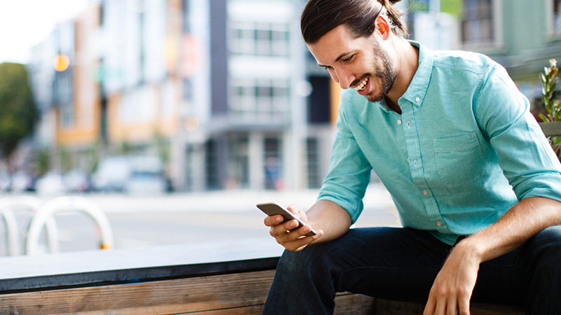 Man using mobile phone while seated outside in a city.